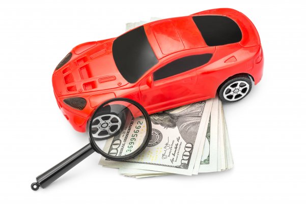 root car insurance price cost red car magnifying glass over dollar bills white background